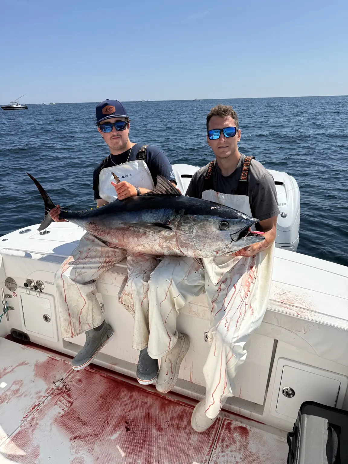 Two anglers holding a large bluefin tuna aboard the boat
