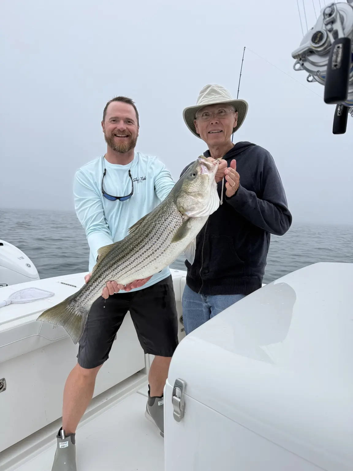 Two anglers displaying a striped bass on a foggy day