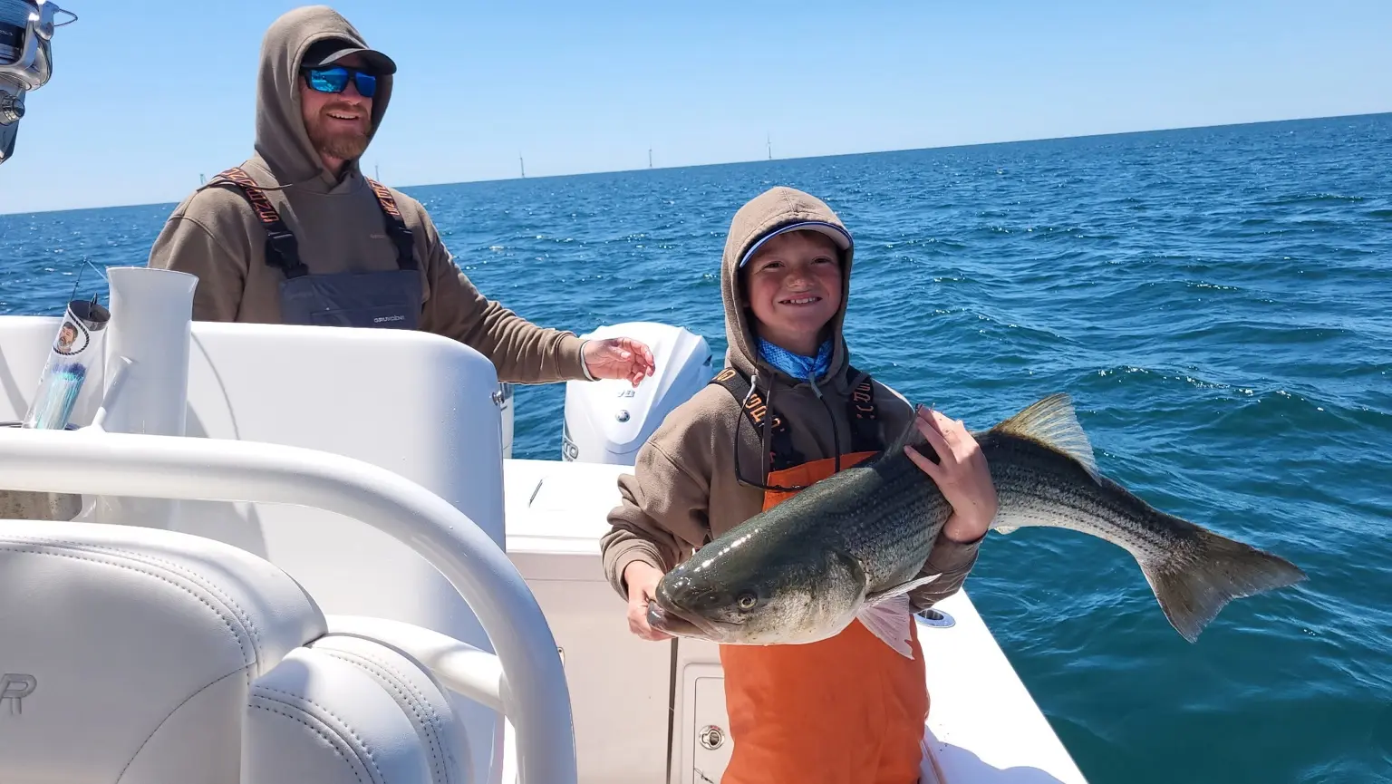 Young angler holding a striped bass on open water